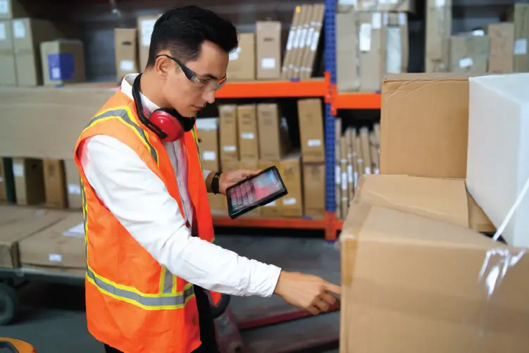 A warehouse worker using a tablet to check and organize packages for freight services from Canberra to Sydney.