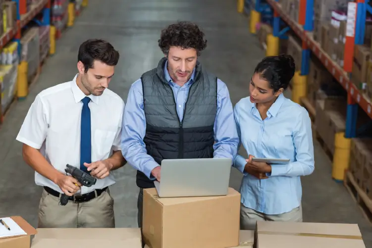 A team of logistics professionals collaborating in a warehouse, using a laptop and barcode scanner to manage freight operations efficiently