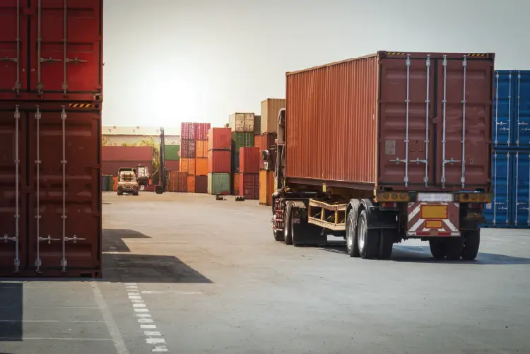 Container truck transporting cargo through a busy freight yard, surrounded by stacked shipping containers.