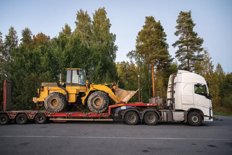 A heavy-duty truck transporting a large yellow wheel loader on a flatbed trailer, showcasing reliable heavy haulage services for businesses in South Australia