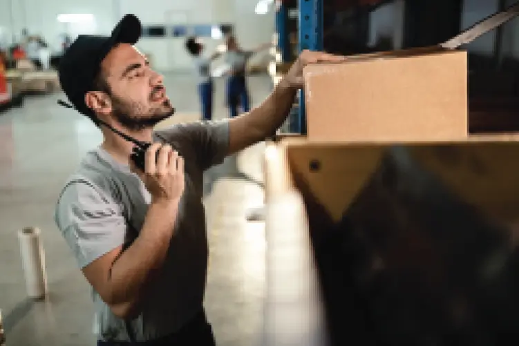 A warehouse worker using a walkie-talkie while handling a package, ensuring efficient same-day delivery from Canberra to Sydney.