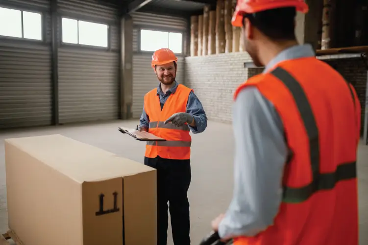 Two warehouse workers discussing a large package in a storage facility, ensuring efficient freight handling.
