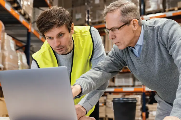 Two logistics professionals reviewing freight data on a laptop in a warehouse, highlighting reliable freight services in South Australia