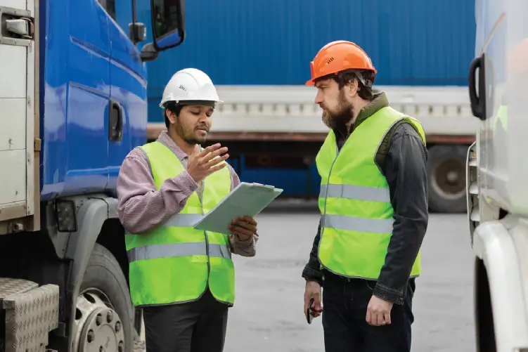 Two freight workers discussing logistics near transport trucks